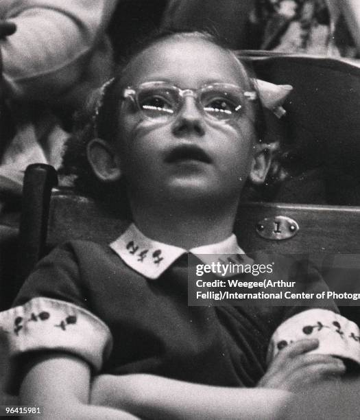 View of circus audience members, including a close-up of a young girl wearing glasses looking up in anticipation of a stunt, New York, ca.1950s.