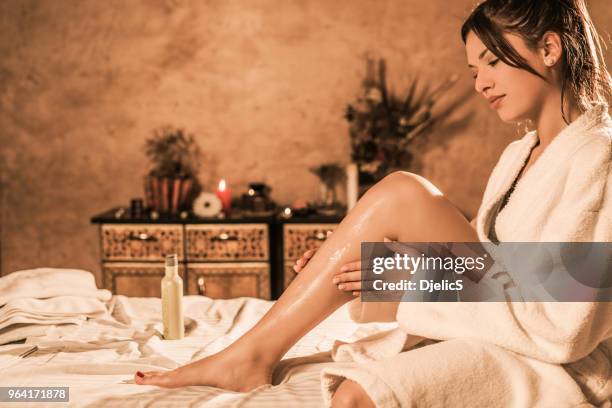 mooie ontspannen jonge vrouw in badjas lotion op haar huid zetten. - blank room stockfoto's en -beelden