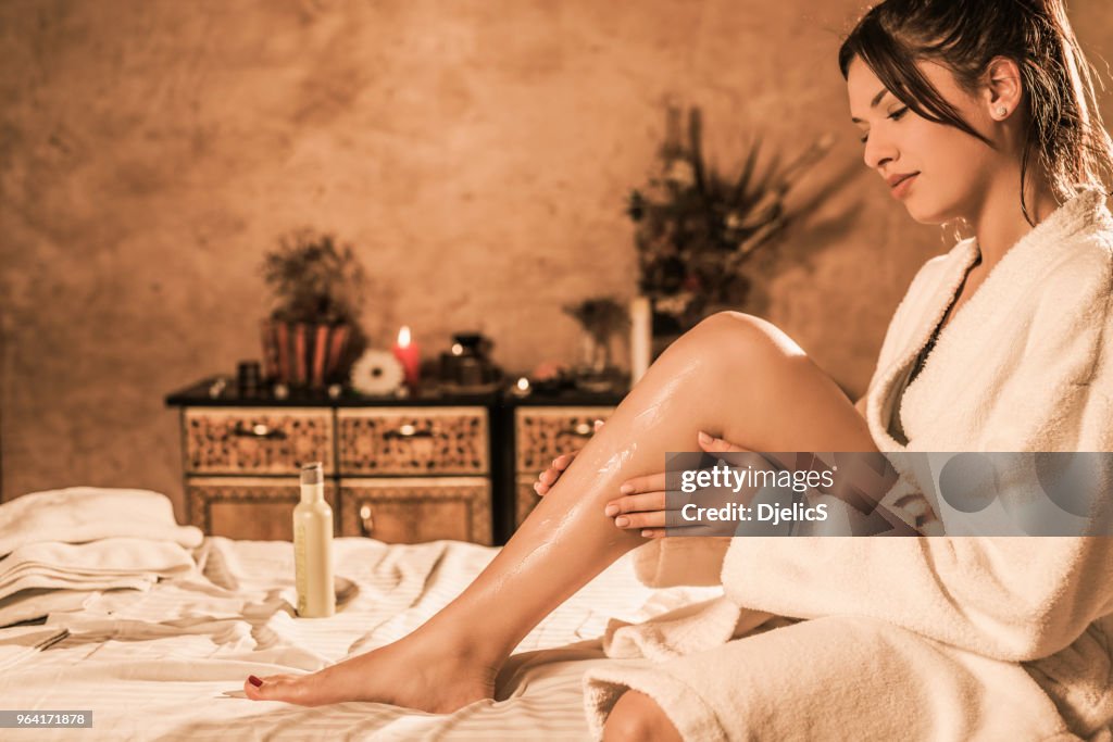 Bela jovem relaxada no roupão de banho colocar a loção na pele dela.