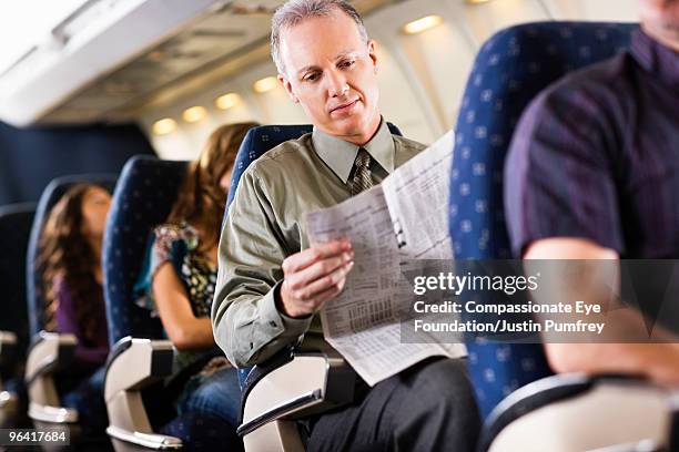 man reading newspaper on airplane - airplane seat stock pictures, royalty-free photos & images