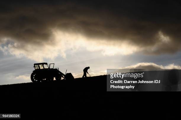 silhouette of farmer working next to his tractor up high in the clouds - low effort stock pictures, royalty-free photos & images
