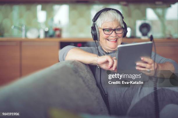 senior vrouw thuis luisteren muziek - oudere internetgebruiker stockfoto's en -beelden