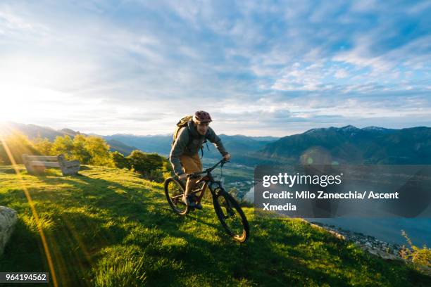 mountain biker follows alpine track, down mountainside - mountain bike foto e immagini stock