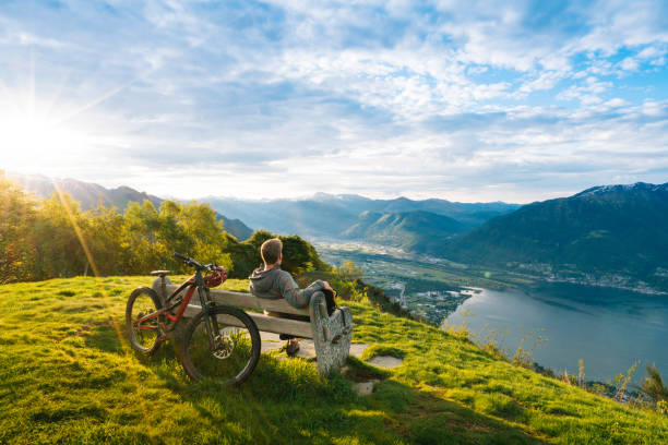 mountain biker relaxes to enjoy view over mountains, lake - 休む ストックフォトと画像