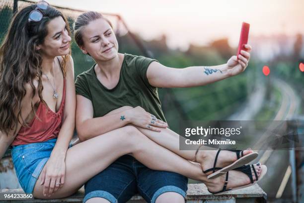 female couple sitting at the overpass in the city and making selfies - white dragon tattoo stock pictures, royalty-free photos & images