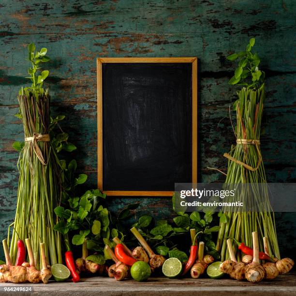 frisse thaise tom yam soep kruiden en specerijen tegen een turquoise gekleurde houten pagina, met een houten frame schoolbord in het midden tussen de bossen van citroengras. - kafferlimoen stockfoto's en -beelden