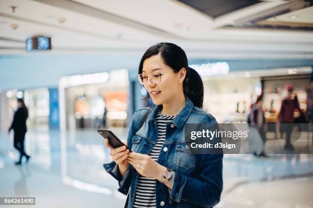 young woman using smartphone in shopping mall - chinese young adults shopping imagens e fotografias de stock