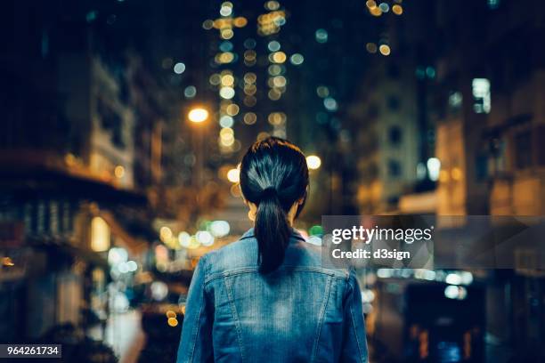 rear view of female traveller exploring city streets and enjoying night scene of hong kong - ergens overheen kijken stockfoto's en -beelden