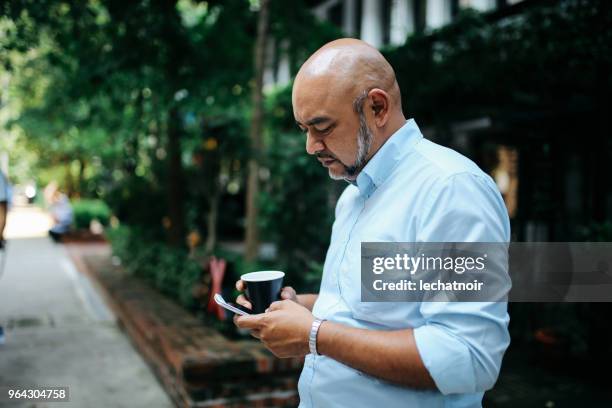 envoyer des sms sur le téléphone portable dans les rues de kuala lumpur homme asiatique d’âge moyen - un seul homme dâge moyen photos et images de collection