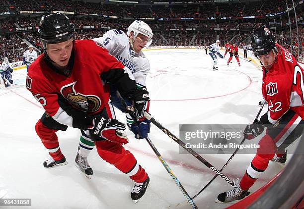 Chris Neil and Chris Kelly of the Ottawa Senators dig for a loose puck in the corner against Christian Ehrhoff of the Vancouver Canucks at Scotiabank...