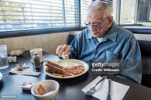 朝食の卵に食卓塩を振りかけるシニア大人老人 - salt shaker ストックフォトと画像