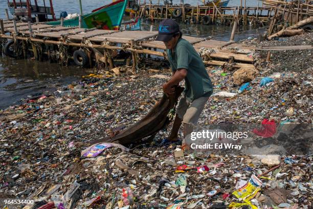 Man wrestles a piece of driftwood onto a beach polluted with plastic waste at a fishing village on the northern coast on May 31, 2018 in Jakarta,...