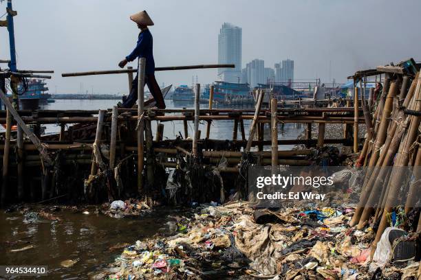 Man walks past a mound of plastic waste left on the shoreline of a fishing village on May 31, 2018 in Jakarta, Indonesia. Indonesia has been ranked...