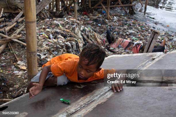 Boy plays with a toy skateboard along a beach which has been covered in plastic waste at a fishing village on May 31, 2018 in Jakarta, Indonesia....