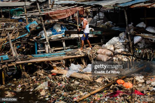 Man carries scrap wood to his boat past mounds of plastic in the water of a fishing village on May 31, 2018 in Jakarta, Indonesia. Indonesia has been...