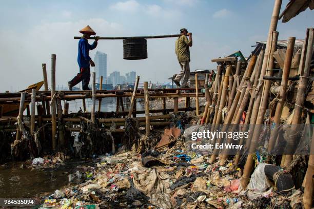 Men unload mussels from a fishing boat, walking past a mounds of plastic waste left on the shoreline of a fishing village on May 31, 2018 in Jakarta,...