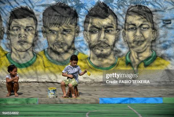 Boy paints the kerb with the Brazilian colours as a girl looks on close to a graffiti showing Brazilian football players taking part in the upcoming...