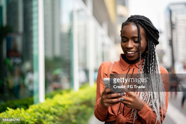 donna afro che usa il cellulare in strada - donna sorride cellulare foto e immagini stock