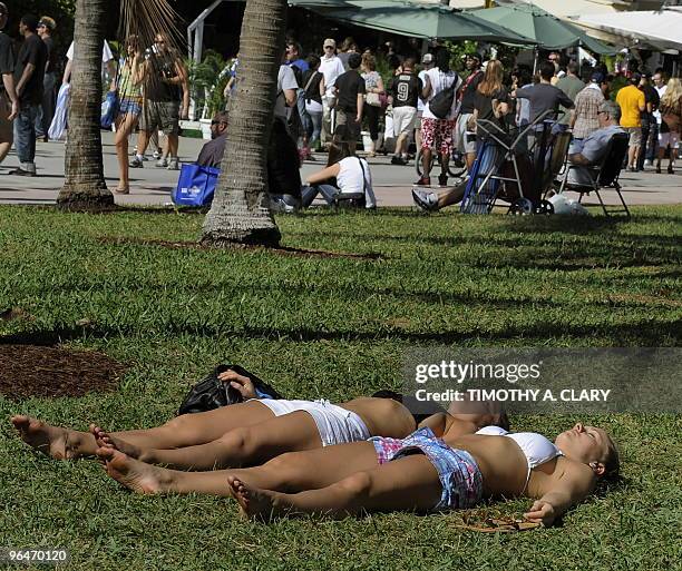 Two woman sunbath as fans stroll down Collins Avenue on South Beach in Miami February 6, 2010. South Florida will host the Indianapolis Colts and the...