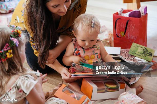 child unwrapping presents with help from her mother at first birthday party - eerste verjaardag stockfoto's en -beelden