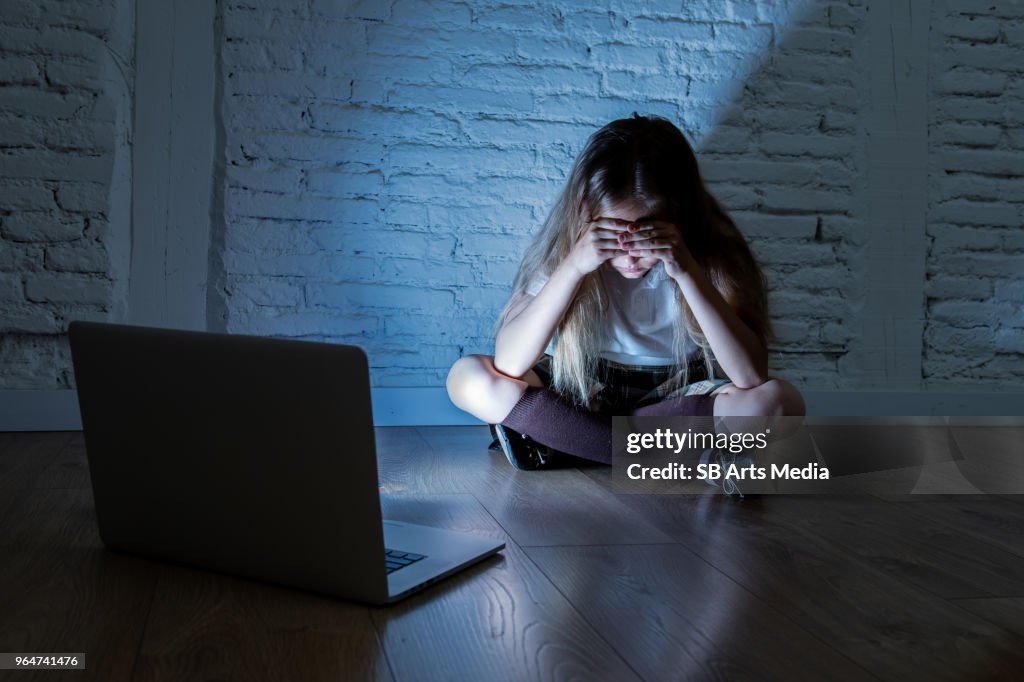 Scared sad girl bullied on line with laptop suffering cyberbullying and harassment feeling desperate and intimidated. Child victim of bullying stalker social media network