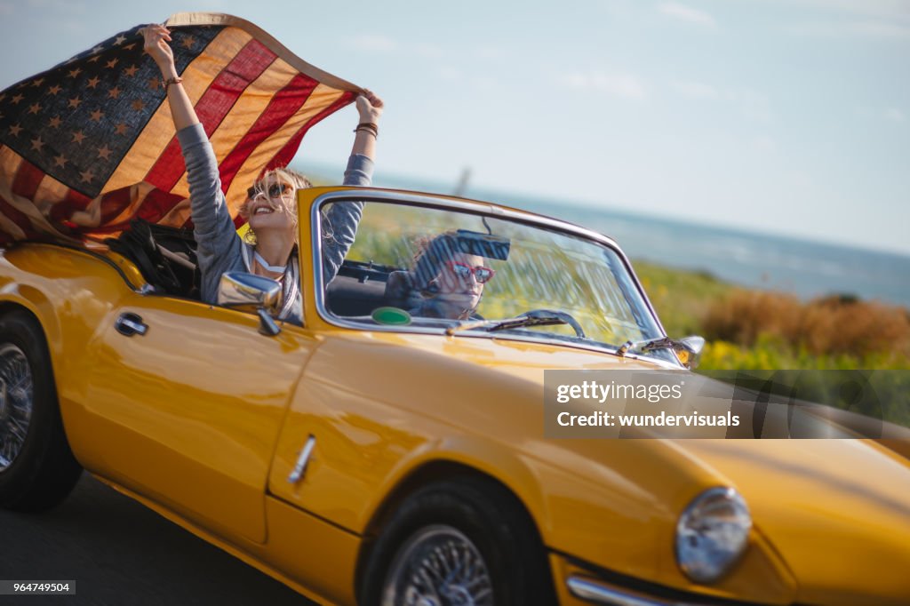 Young hipster women with American flag driving retro convertible car