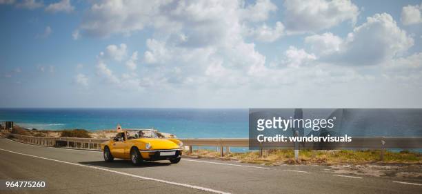 young women driving retro convertible car on seaside highway - classic car stock pictures, royalty-free photos & images