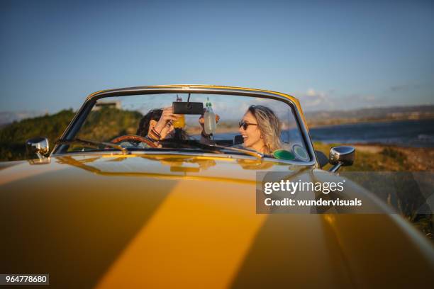 hipster women with vintage convertible car drinking soda at beach - drinking soda in car stock pictures, royalty-free photos & images