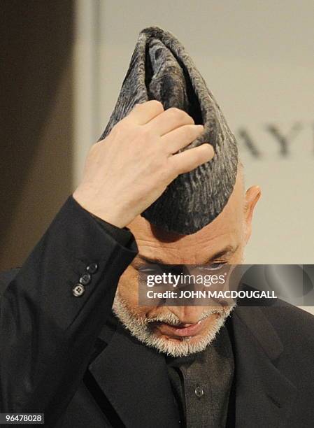 Afghan President Hamid Karzai takes off his hat before addressing participants prior to a panel discussion on Afghanistan at the 46th Munich Security...