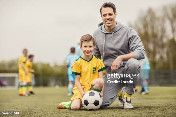 father and son soccer players posing for photo during a football training session - family football team stock pictures, royalty-free photos & images