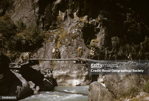 Bridge over Dudh Kosi, laborers, nearing the end of their journey cross a wooden bridge over the Dudh Kosi in the Khumbu region. These bridges are...