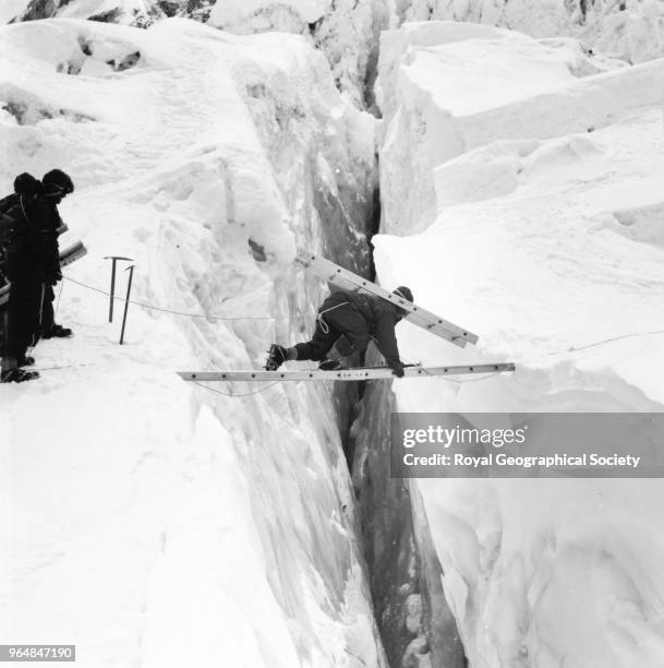 Sherpa carrying a ladder section across ladder bridge on the icefall, Sherpa carrying a ladder section across ladder bridge on the icefall between...