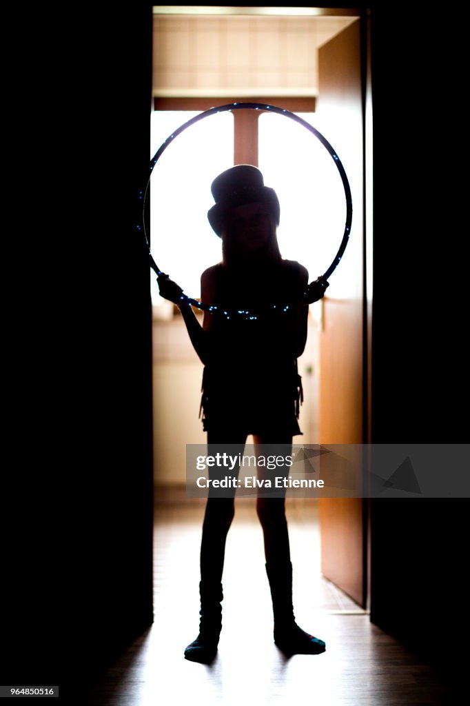 Silhouette of girl dressed up as a magician, standing in a backlit doorway, holding a hoop