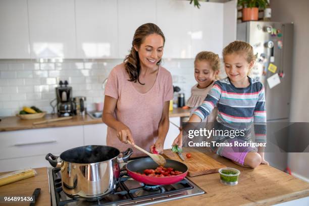 woman cooking with twin girls in a kitchen - gas stoves stock pictures, royalty-free photos & images