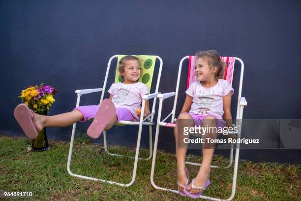 little twin girls sitting on garden chairs - leg stretch girl stock pictures, royalty-free photos & images