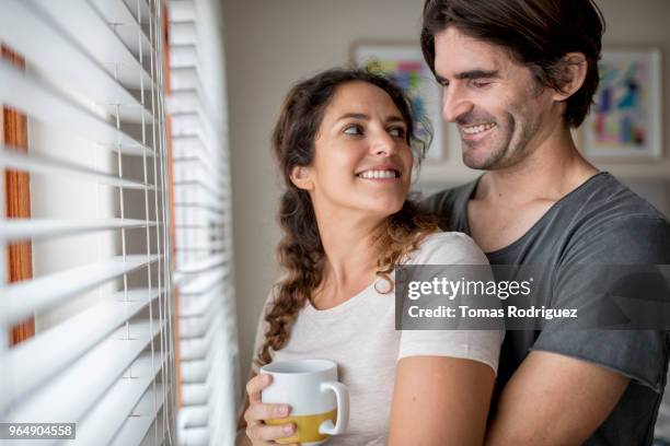 happy couple embracing next to window - jalousie window stock pictures, royalty-free photos & images