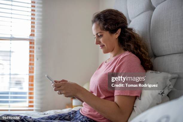 young woman on bed using mobile phone - jalousie fotografías e imágenes de stock