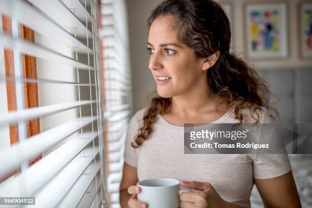 portrait of young woman looking out a window - jalousie stockfoto's en -beelden
