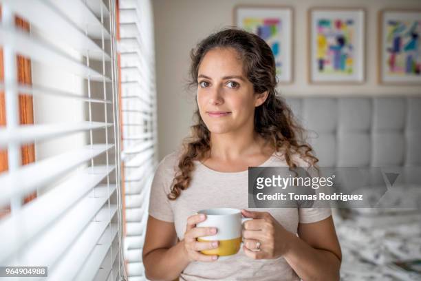 portrait of young woman standing next to window - jalousie stockfoto's en -beelden