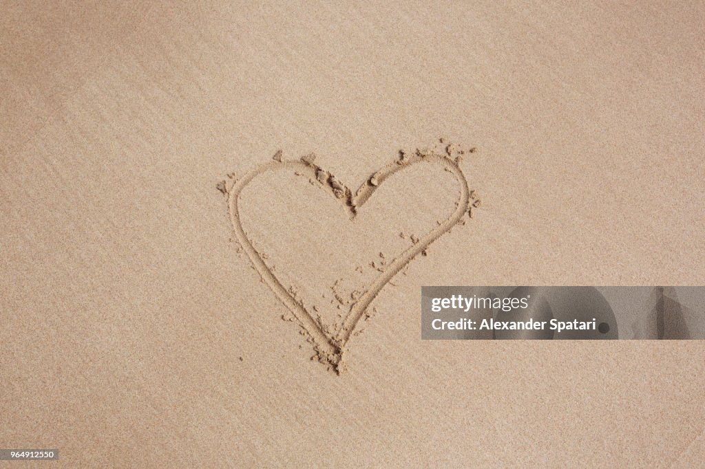 Heart shape drawing made with finger on a sand of the beach