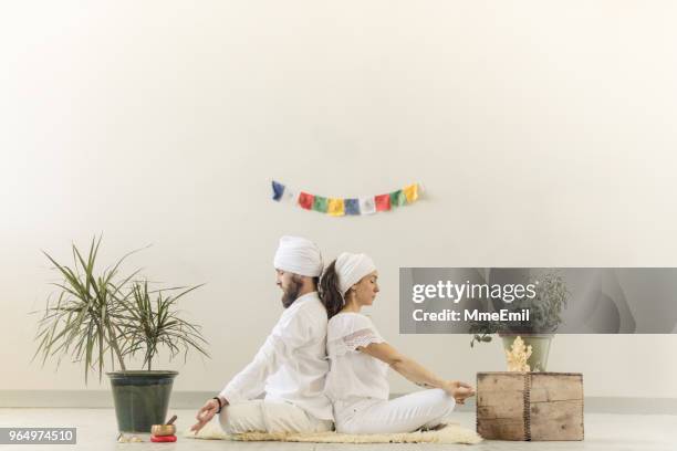 couple practicing kundalini yoga and meditating back to back - new age stock pictures, royalty-free photos & images