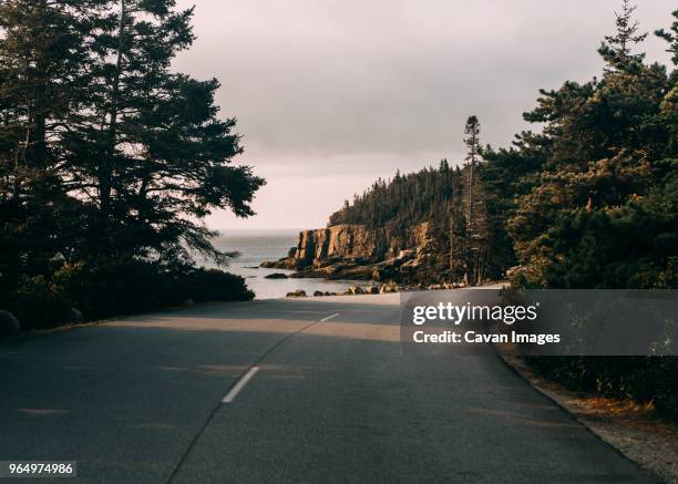 country road by sea against cloudy sky - maine road stock pictures, royalty-free photos & images