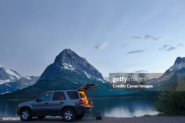 sports utility vehicle parked on shore of swiftcurrent lake against mt. grinnell - suv stockfoto's en -beelden