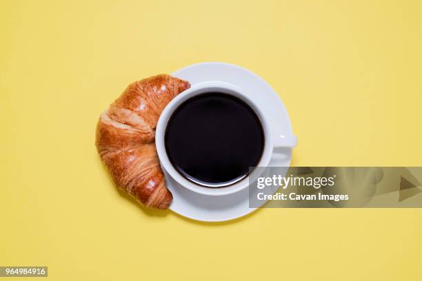 overhead view of black coffee and croissant on yellow table - croissant foto e immagini stock