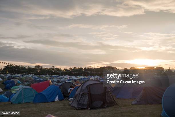 tents on field against cloudy sky at campsite during sunset - abundance stock-fotos und bilder