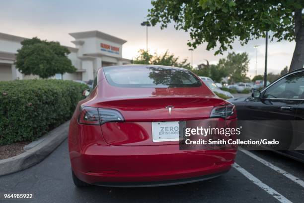 Rear view of a red Tesla Model 3 electric car from Tesla Motors with a license plate reading Zero Emissions under a dramatic sky in the San Francisco...