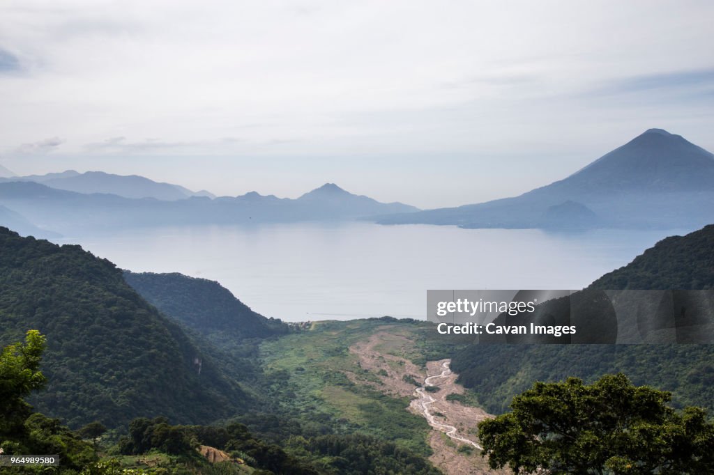 High angle scenic view of Lake Atitlan amidst mountains against cloudy sky during foggy weather