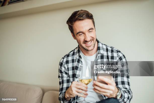 young man using phone and drinking wine at home - letting it all hang out stock pictures, royalty-free photos & images