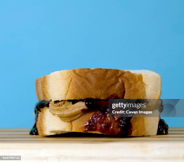 close-up of peanut butter and jam in bread on table against blue background - peanut butter and jelly sandwich stock pictures, royalty-free photos & images