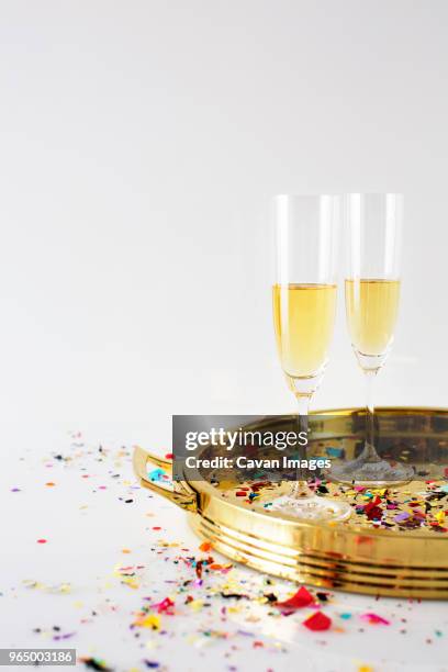 champagne flutes in tray with confetti on table against white background - champagne or photos et images de collection